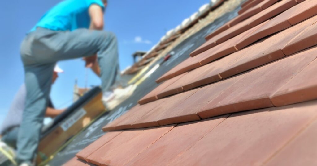 Deux couvreurs installent une toiture de tuiles en terre cuite plate sur une toiture en pente. 