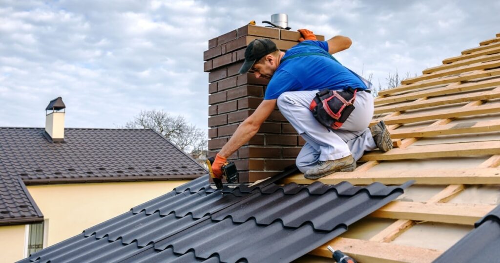 Un couvreur sur un toit de maison installe une couverture en plaques ondulées à l'aide d'une perceuse. 