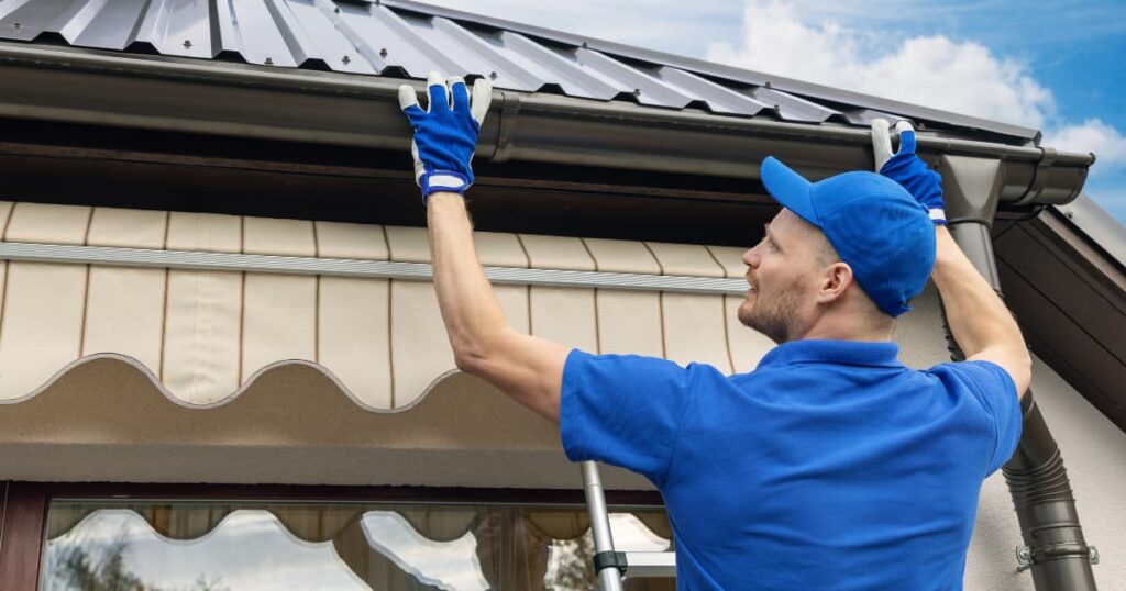 ouvrier en train de placer une gouttiere sur un toit en tôle