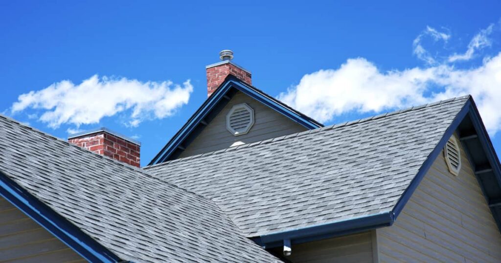 Une maison avec des tuiles grises et une cheminée en brique rouge sous un ciel bleu avec quelques nuages