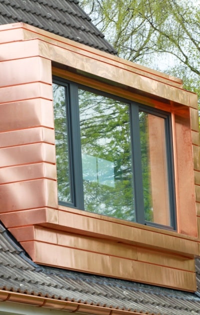 Fenêtre encadrée de cuivre sur un toit brun avec des arbres en fond. 