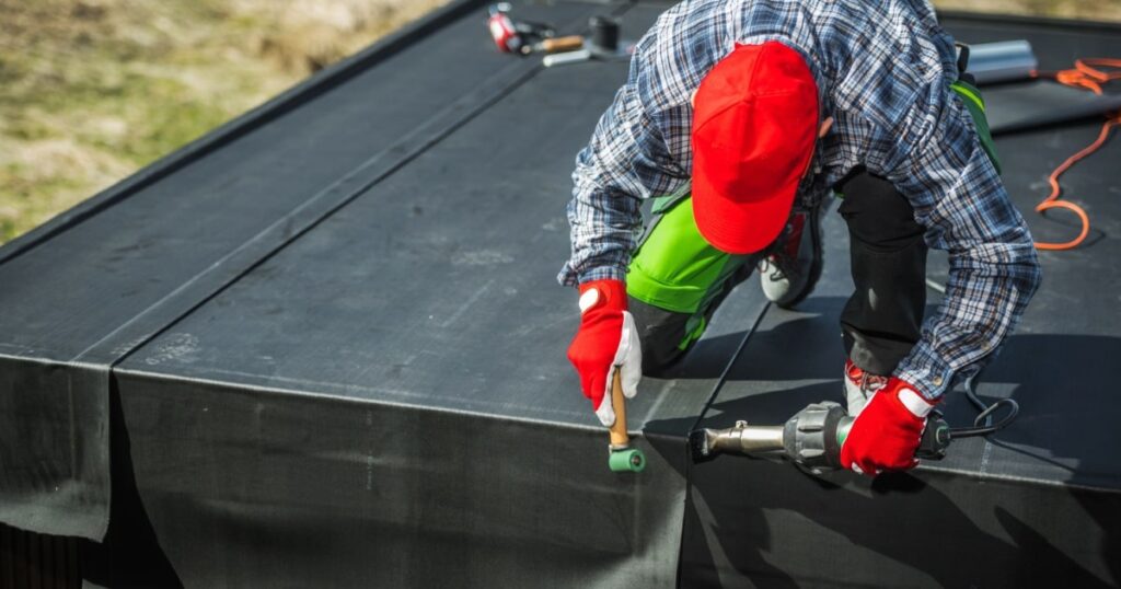 Un ouvrier pose un revêtement EPDM sur une toiture plate. 