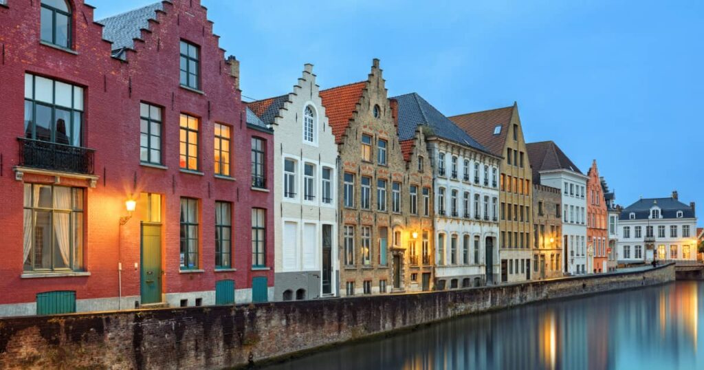 Plusieurs maisons de couleurs différentes, le long d'un canal, dans la ville de Bruges avec toits en pente 