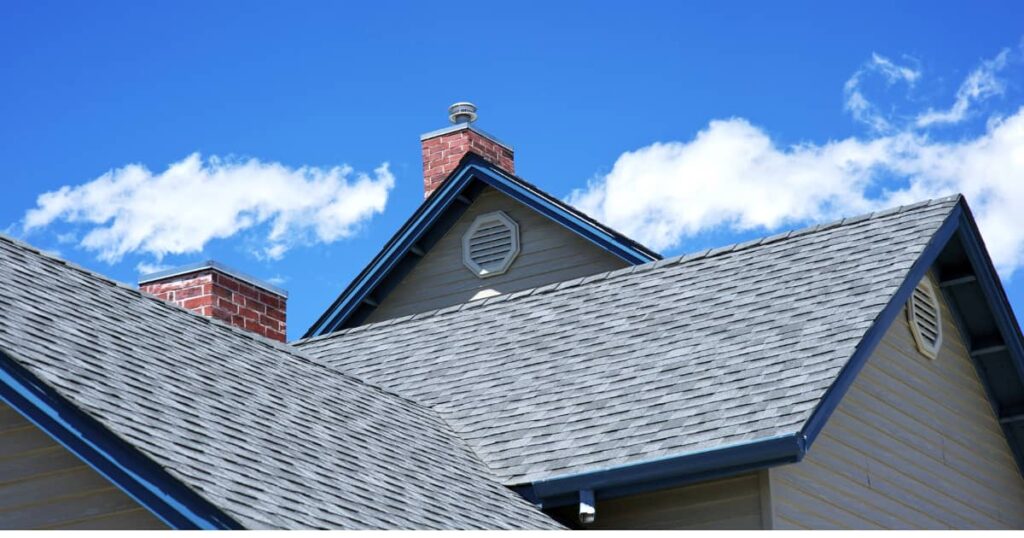 Une maison avec tuiles grises et toiture inclinée sous un ciel nuageux